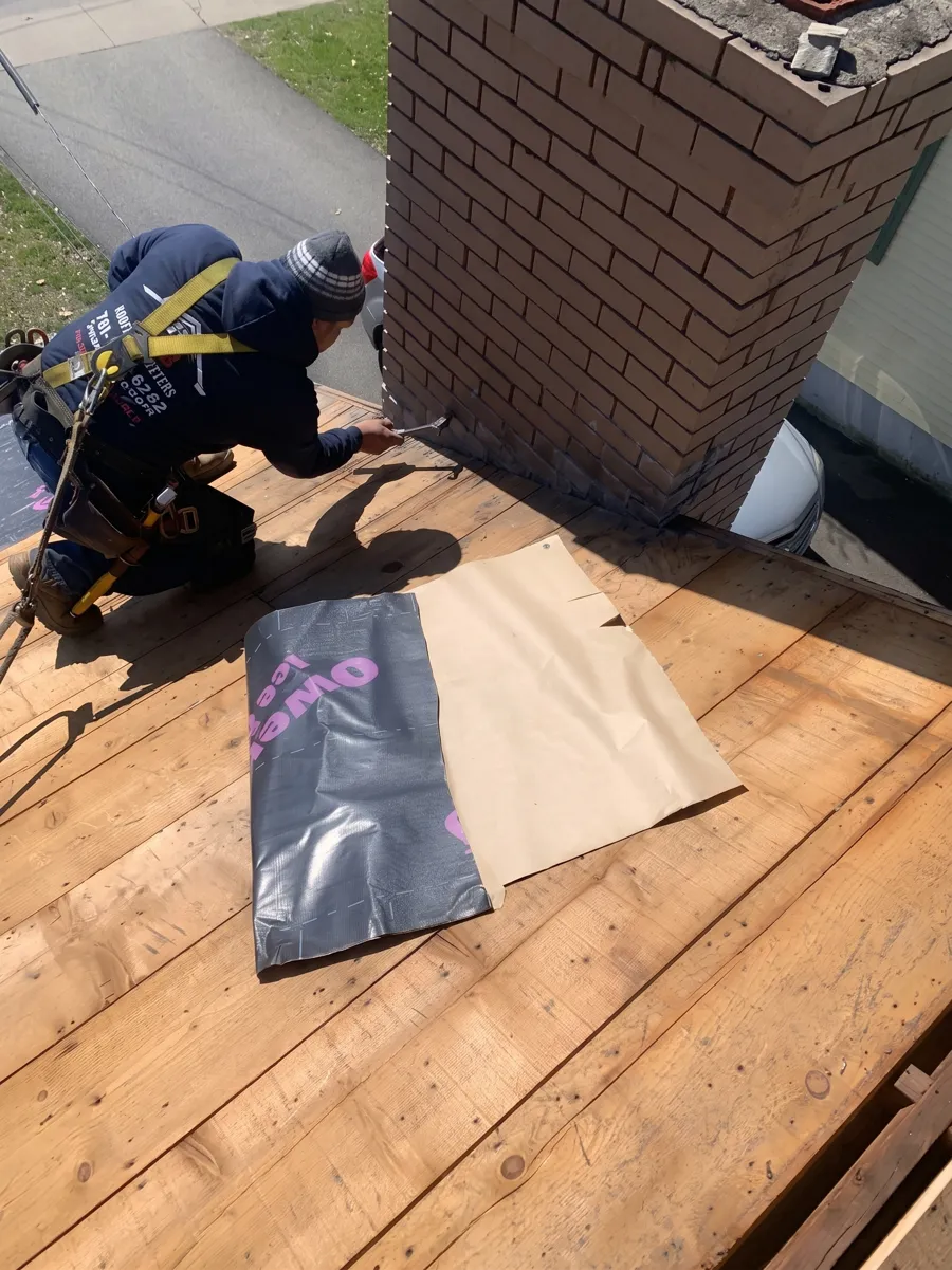 Roofer flashing a brick chimney on a new roof deck